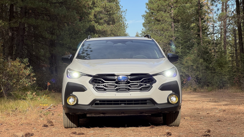 Un plan frontal de l'hybride White Crosstrek avec ses phares sur des aiguilles de pin devant les arbres