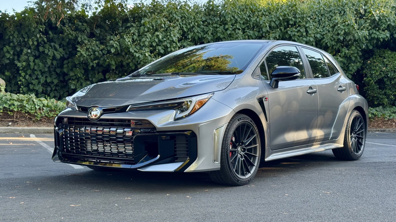 Une prise de trois quarts avant d'une Corolla Silver GR dans un parking devant les haies