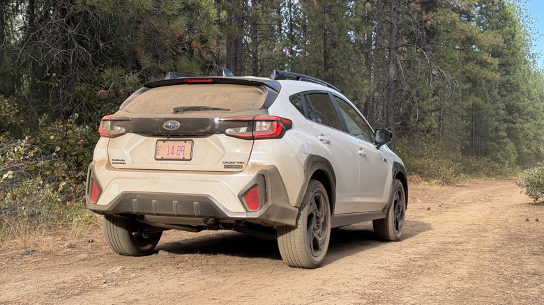 Un tir arrière à trois quarts de l'hybride Crosstrek blanc très poussiéreux garé sur la saleté devant les arbres